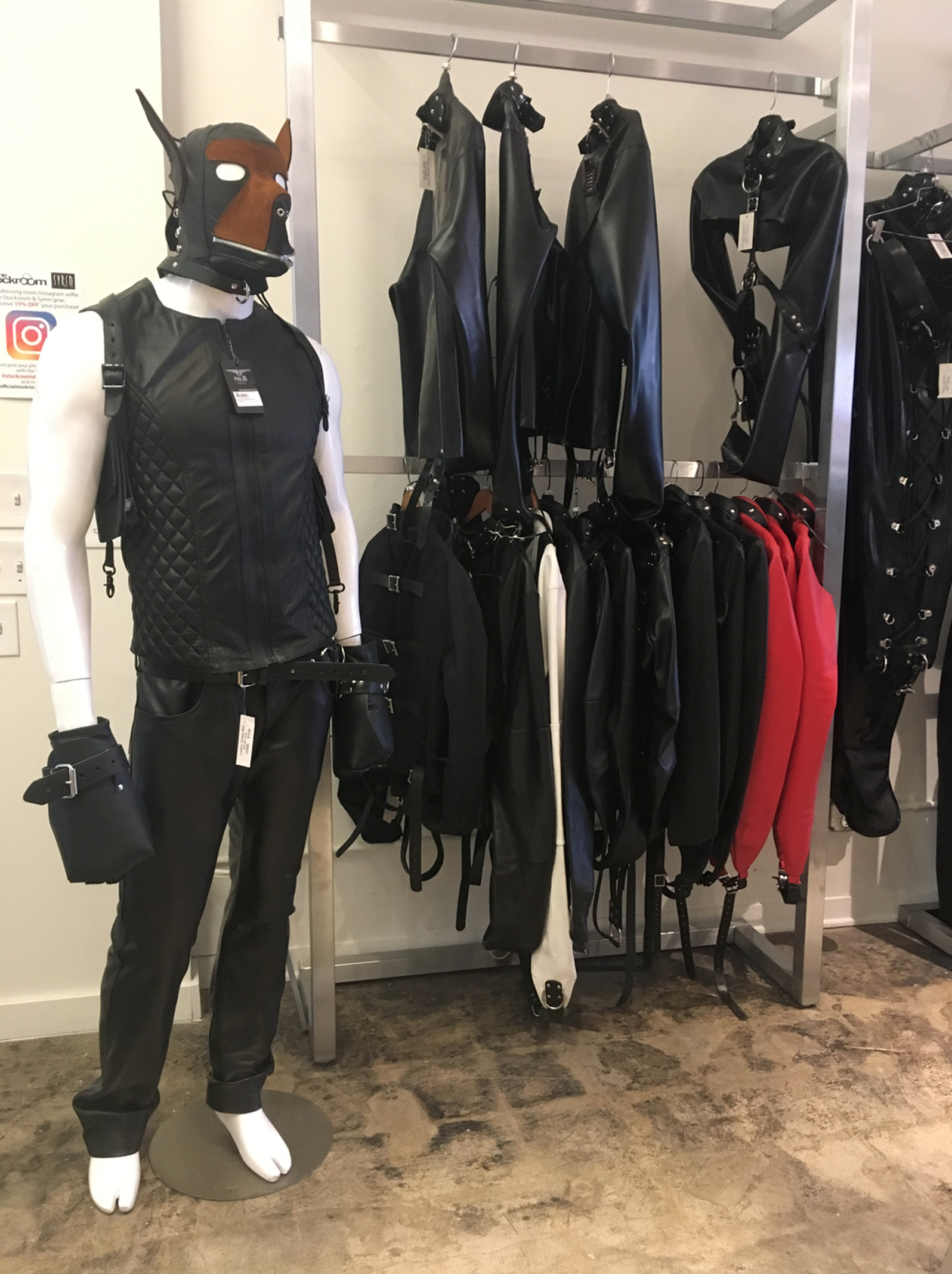 A mannequin wearing a furry mask and tight leather clothing. Beside it is a rack of leather harnesses and clothing.